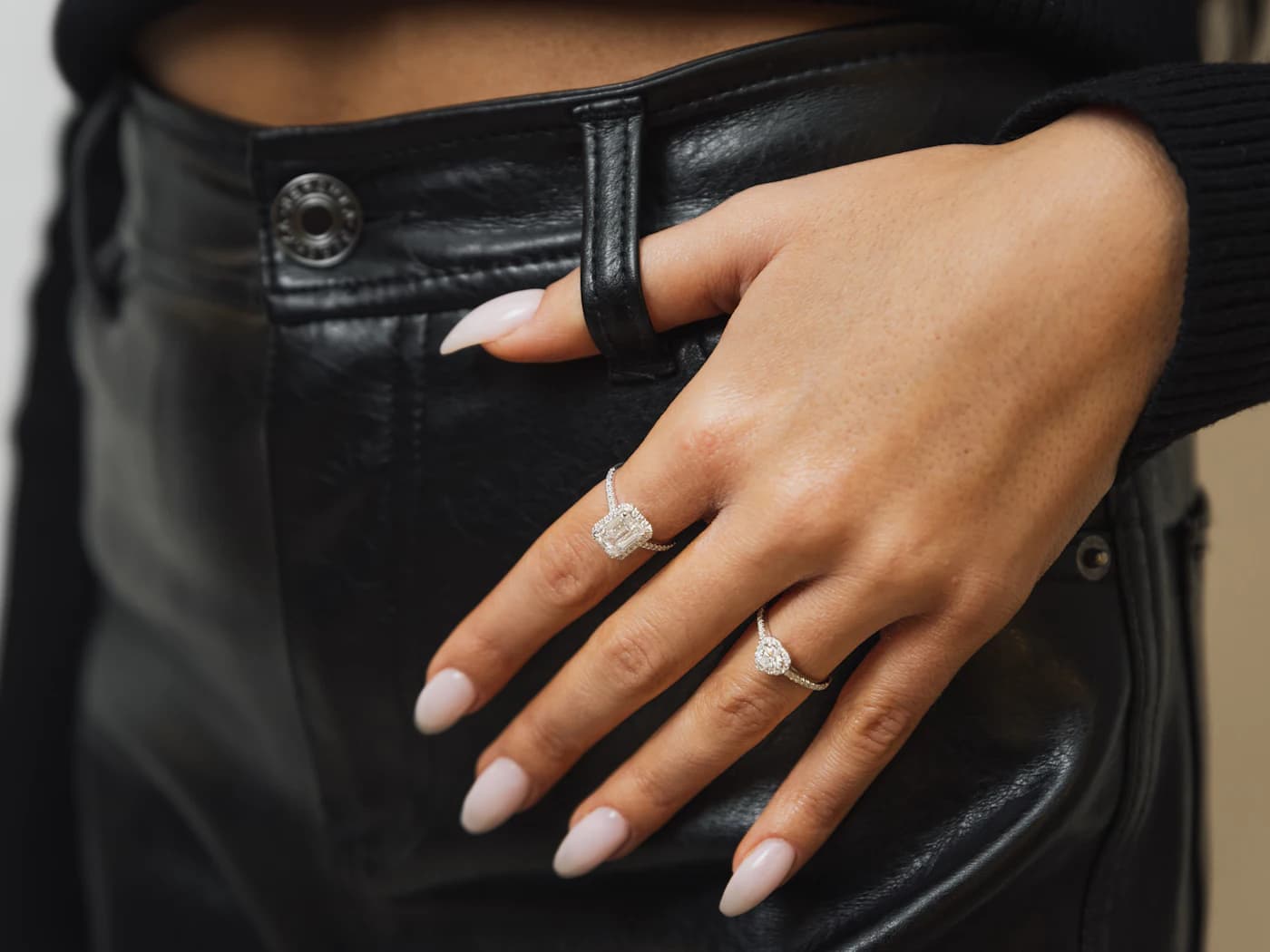 Hands wearing diamond rings against black leather